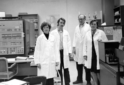 Margaret Oakley Dayhoff in the computer room at the National Biomedical Research Foundation, in front of the punch card reader.  Margaret Dayhoff created the first large scale database of protein sequences, and developed many of the early algorithms for a