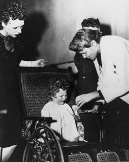 Helen Taussig examining a child, her large boxed hearing aid is next to the child, ca. 1947 